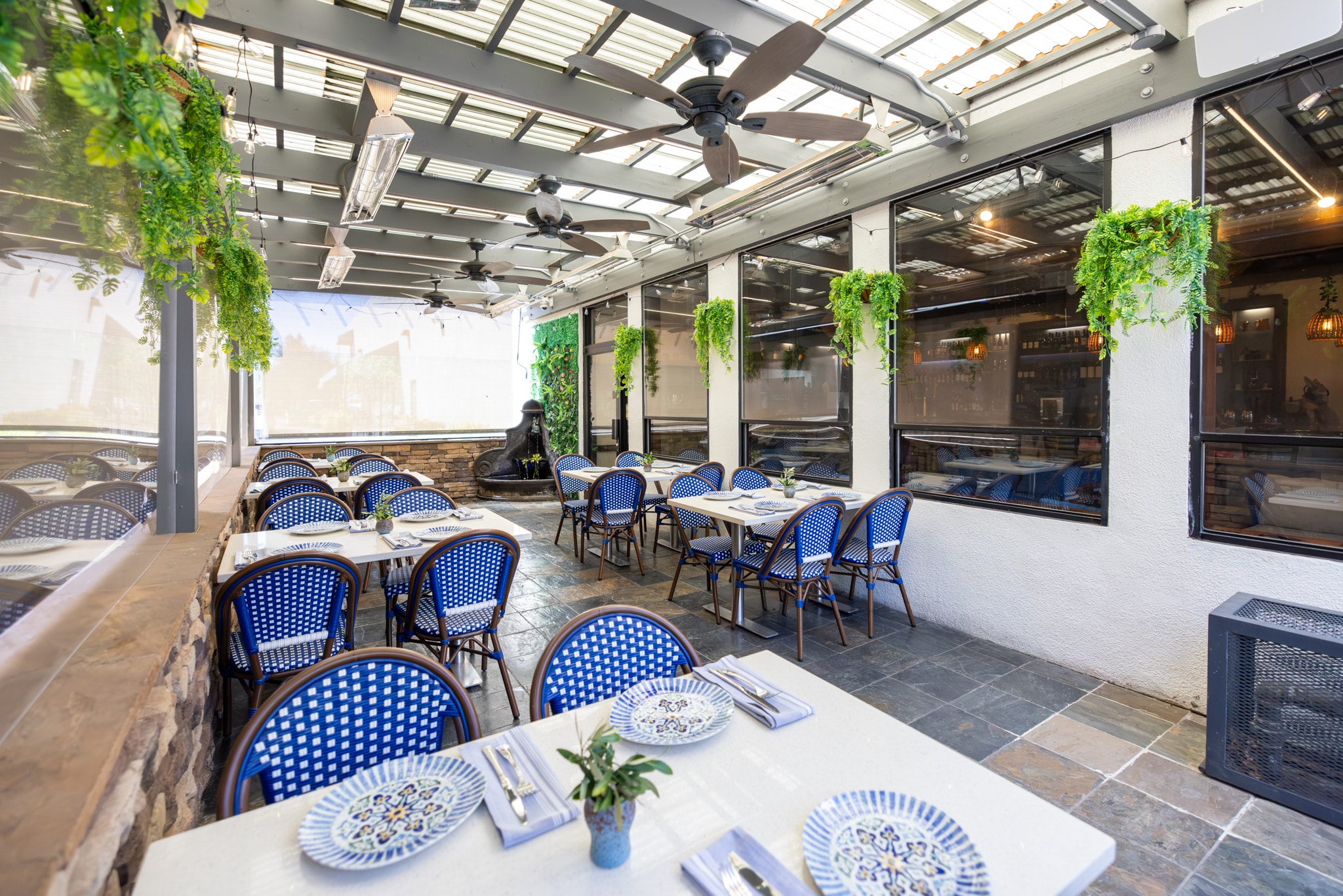 Covered patio dining room with blue bistro chairs and hanging greenery